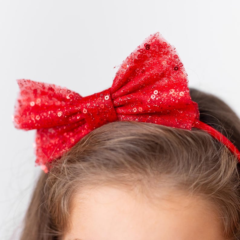 Close-up of a red sparkly bow headband styled with a red satin flower girl dress for a Christmas holiday look.