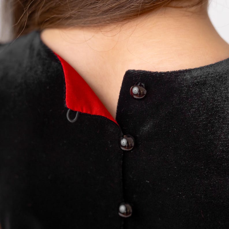 Close-up of the back button closure and red lining detail on a red and black sparkly Christmas holiday flower girl dress.