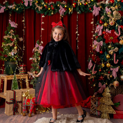 Girl wearing a red and black sparkly Christmas holiday dress styled with a black faux fur cape in a festive decorated setting.”