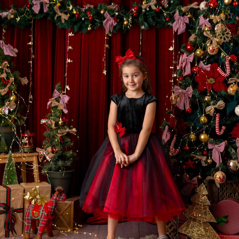Girl standing in a red and black sparkly Christmas holiday dress with a velvet bodice and layered tulle skirt, classic festive backdrop.