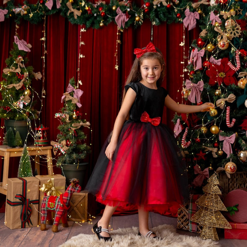 Girl posing beside a Christmas tree in a red and black sparkly Christmas holiday dress with a velvet bodice and tulle skirt.