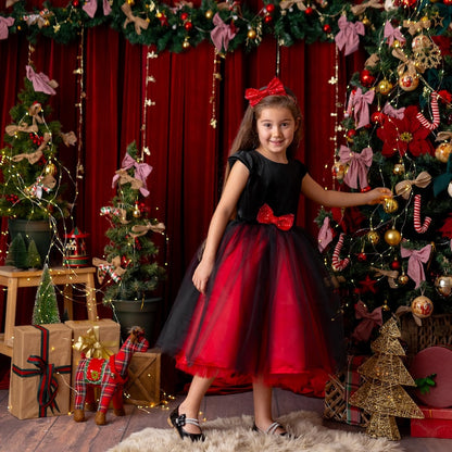 Girl posing beside a Christmas tree in a red and black sparkly Christmas holiday dress with a velvet bodice and tulle skirt.