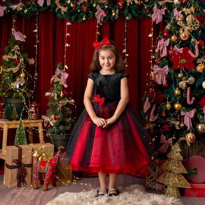 Girl standing centered in a red and black sparkly Christmas holiday dress with a velvet bodice and full tulle skirt, festive decor.