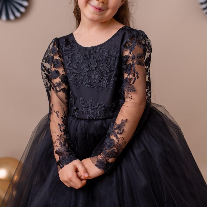 Young girl in a black lace dress, posing with a beige background and decorative accents.