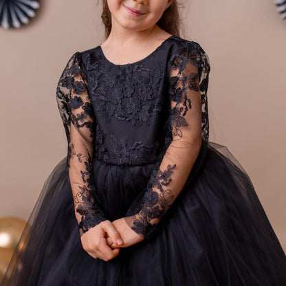 Young girl in a black lace dress, posing with a beige background and decorative accents.