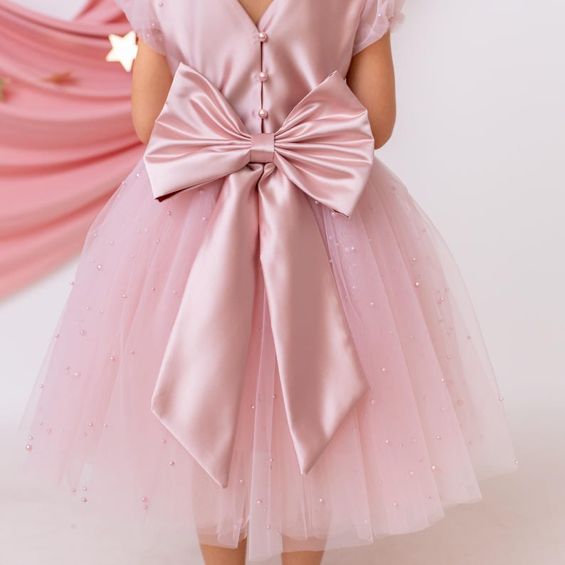 Close-up of the back of a pink flower girl dress with a satin bow, pearl details, and a tulle skirt.