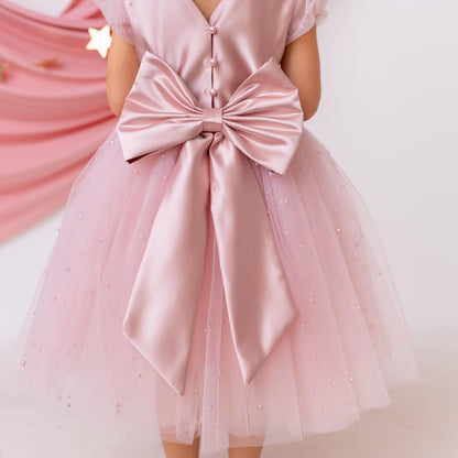 Close-up of the back of a pink flower girl dress with a satin bow, pearl details, and a tulle skirt.