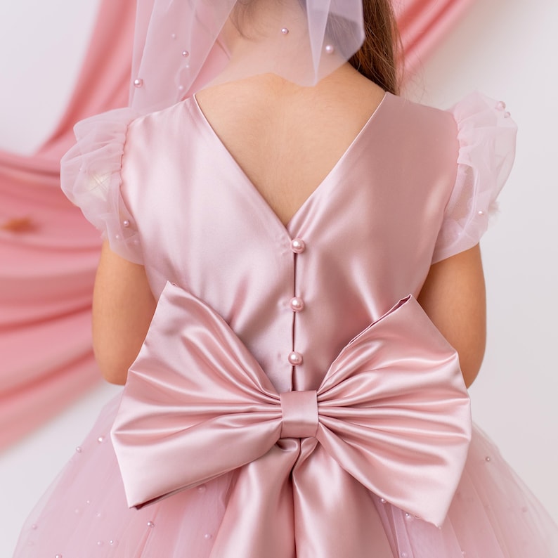 Back view of a pink flower girl dress with satin bow detail and button closure, ideal for special occasions.