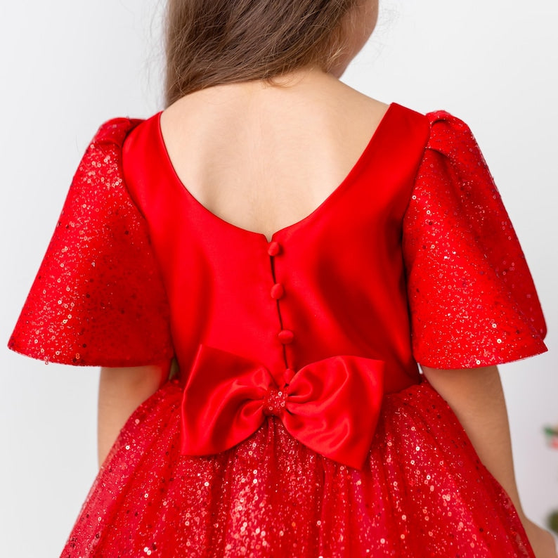 Back view of a red satin flower girl dress with button closure and bow detail, styled as a sparkly Christmas holiday dress.
