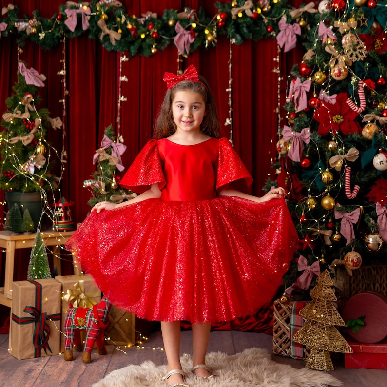 Girl wearing red satin flower girl dress with sparkly tulle skirt in festive Christmas studio
