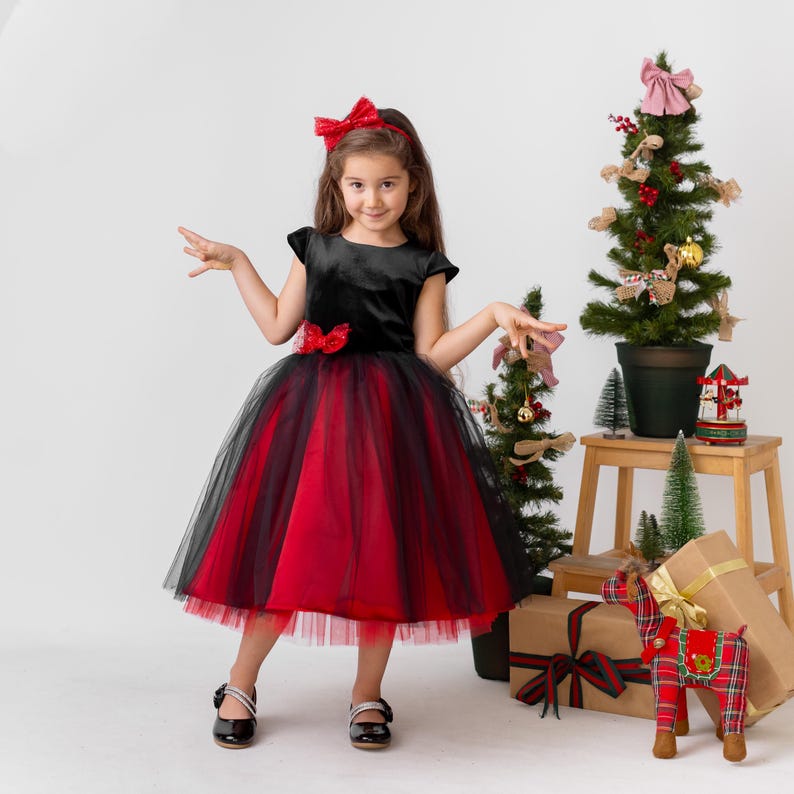Girl wearing a red and black sparkly Christmas holiday dress with a velvet bodice and layered tulle skirt, festive studio setting.