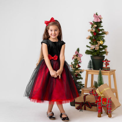 Girl posing in a red and black sparkly Christmas holiday dress with a velvet bodice, bow waist detail, and layered tulle skirt.