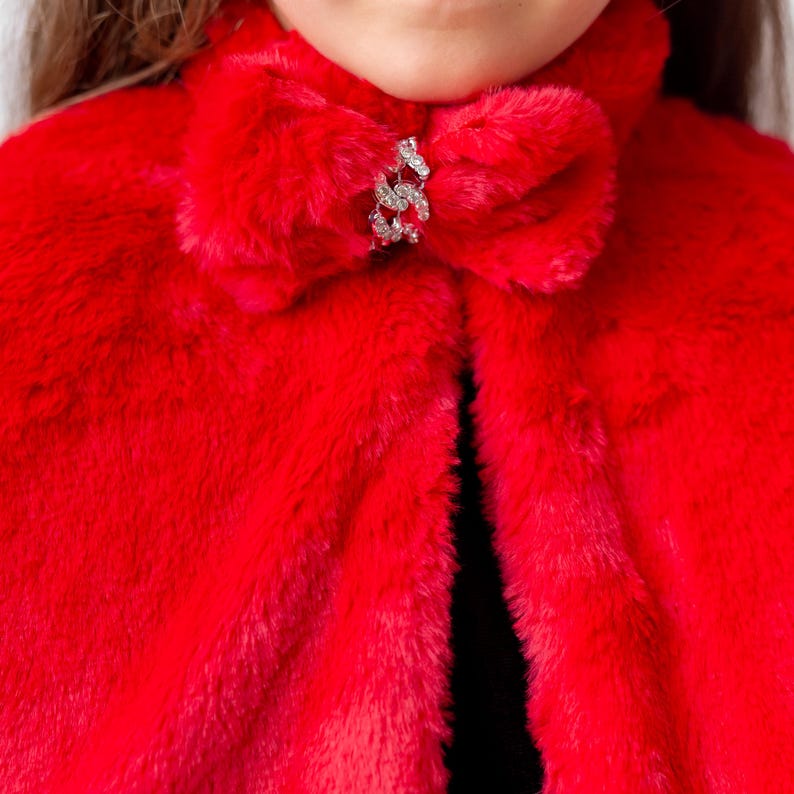 Close up of red faux fur cape bow and jeweled clasp worn over black and red velvet girls dress
