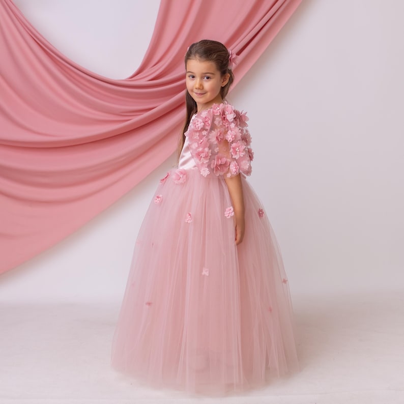 Side view of blush satin flower girl dress showcasing a flowing tulle skirt and textured floral appliqué sleeves