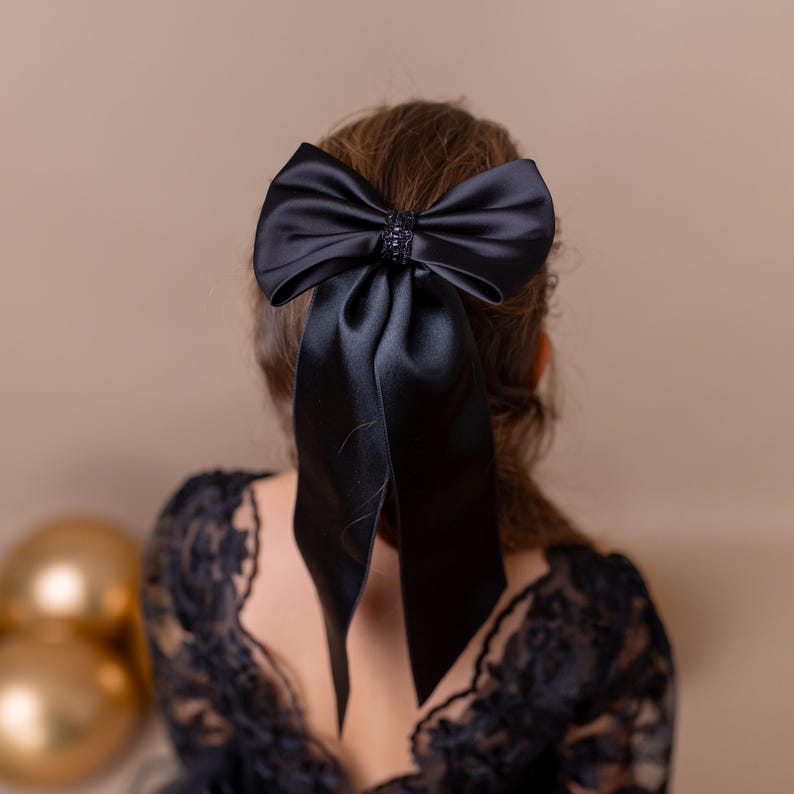 Young girl wearing a large black bow in her hair, set against a neutral beige background.