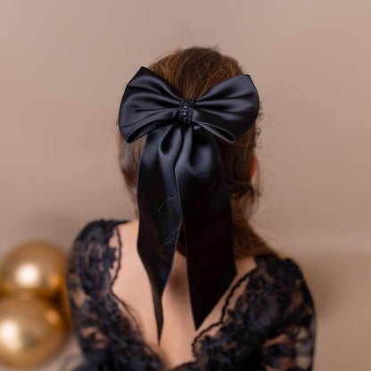 Young girl wearing a large black bow in her hair, set against a neutral beige background.