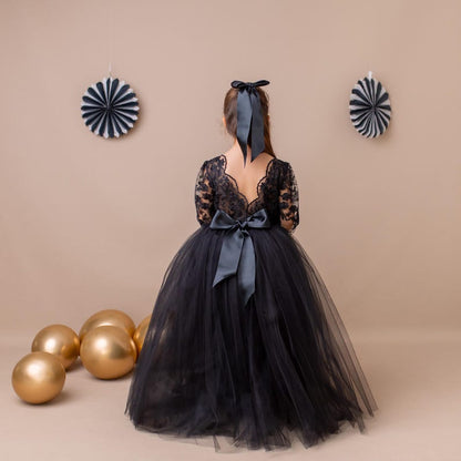 Young girl in a black lace dress with a black ribbon, standing with gold balloons and decorative fans against a beige background.