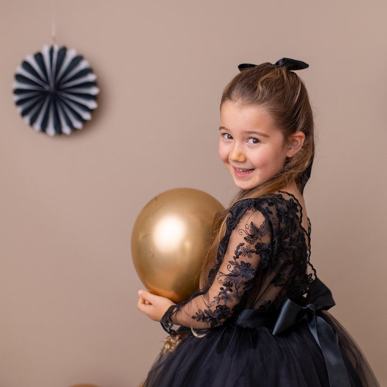 Black lace long-sleeve tulle flower girl dress, shown from the back as a girl holds a gold balloon.