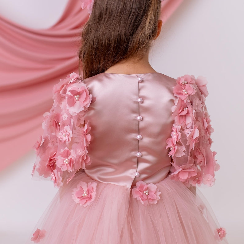 Back view of blush satin flower girl dress featuring pearl button closure and floral appliqué sleeves with soft tulle skirt