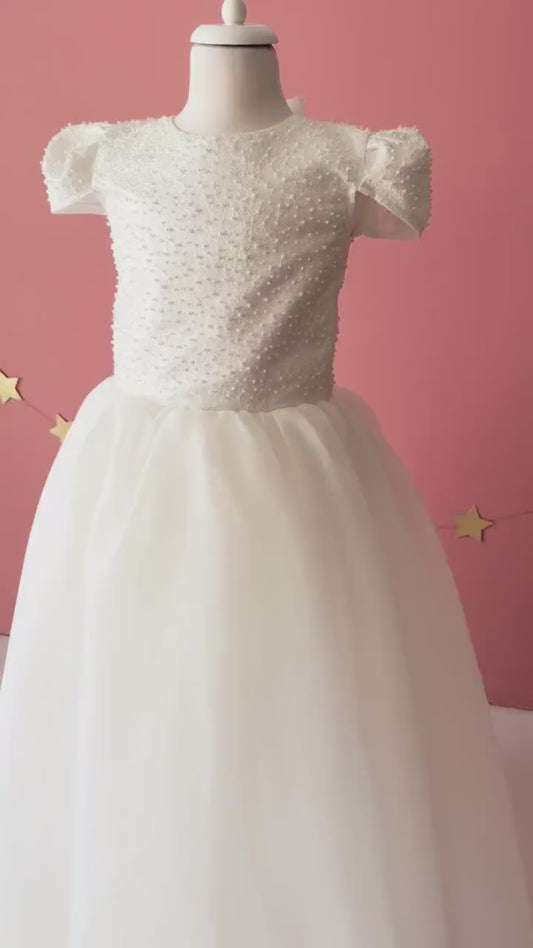 Video of off-white flower girl dress showcasing pearl bodice, bow back detail, and flowing tulle skirt